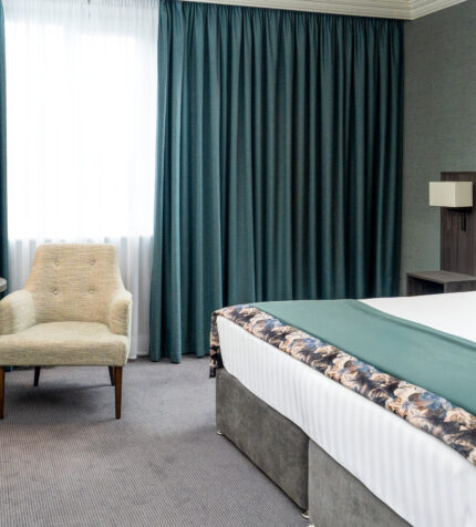 Elegant hotel room with a plush double bed, cosy sitting area, stylish decor, and soft lighting for a relaxing stay.