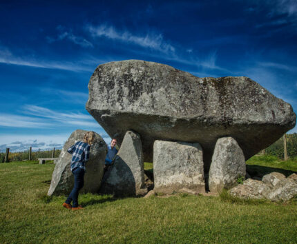 Ancient stone dolmen under a vibrant blue sky with visitors exploring the historic site, perfect for cultural and scenic tours.