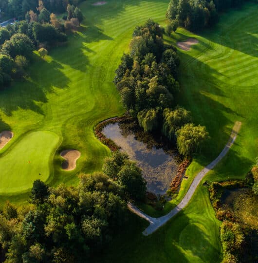 Aerial view of lush green hotel golf course with pristine fairways, tranquil ponds, and cosy forest-side villas.