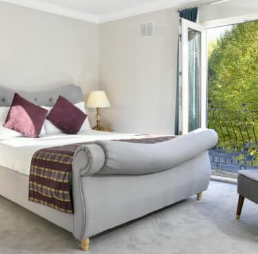 Elegant hotel room with plush grey bed, cosy armchair, and balcony view of lush greenery. Enjoy tranquil comfort and style.