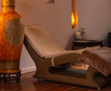 Relaxing spa lounge with comfy wicker chaise longue, warm lighting, and elegant decor, offering a tranquil retreat.