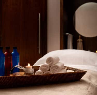 Spa room with treatment table, luxury toiletries, rolled towels, and soothing candlelight for a relaxing experience.