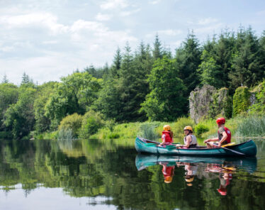 Family canoeing on serene lake surrounded by lush forest, enjoying nature and tranquillity at our peaceful hotel retreat.