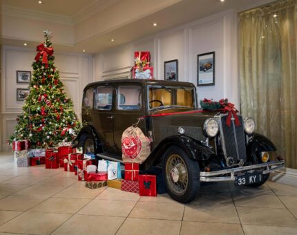 Festive hotel lobby with classic car, adorned Christmas tree, and wrapped presents, creating a warm holiday ambiance.