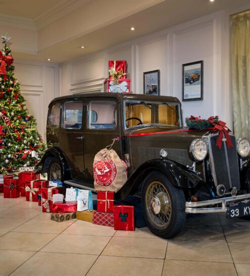 Festive hotel lobby with classic car, adorned Christmas tree, and wrapped presents, creating a warm holiday ambiance.