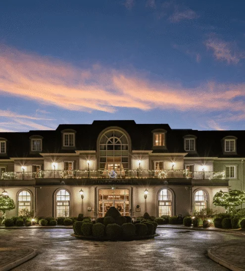 Elegant hotel façade at sunset with warm lighting, manicured gardens, and welcoming entrance in luxurious setting.