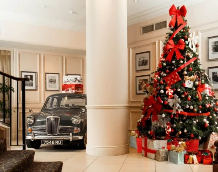 Elegant hotel lobby with vintage car display, festive Christmas tree, grand staircase, providing a luxurious, welcoming ambiance.