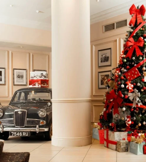 Elegant hotel lobby with vintage car display, festive Christmas tree, grand staircase, providing a luxurious, welcoming ambiance.