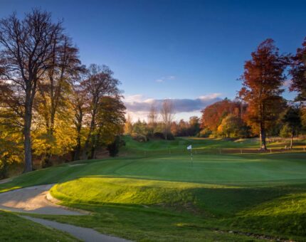 Scenic golf course at sunset with lush green fairways and vibrant autumn trees at luxury countryside hotel.