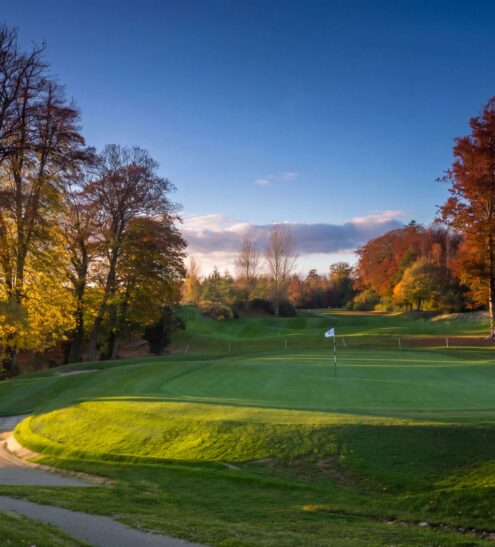 Scenic golf course at sunset with lush green fairways and vibrant autumn trees at luxury countryside hotel.