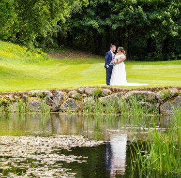 Couple stands by tranquil pond with lush greenery, ideal for weddings and relaxing stays.