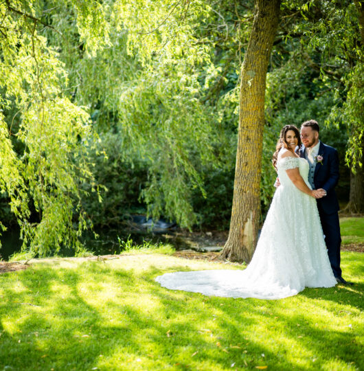 Bride and groom embrace under lush trees on hotel grounds, surrounded by vibrant greenery and serene atmosphere.