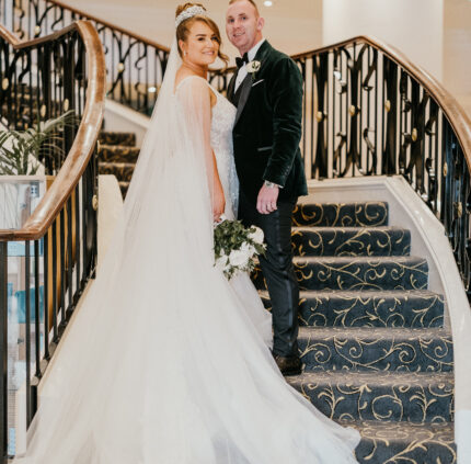 Elegant couple on grand staircase with floral carpet, luxurious decor, ideal for weddings at this stylish hotel venue.