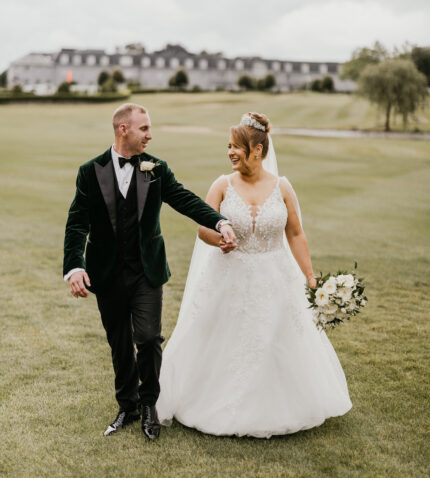 Bride and groom stroll on lush hotel grounds, elegant building in background, perfect for weddings and scenic stays.