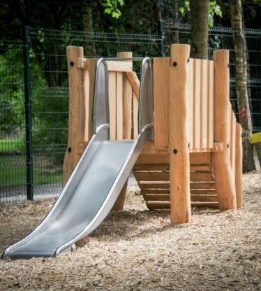 Charming wooden children's play area with a slide in a lush, tree-lined garden, perfect for family-friendly stays.