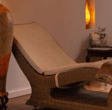Relaxing wicker lounger in cosy spa room with soft lighting, plush cushions, elegant decor, and ambient warmth.