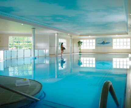 Luxurious indoor pool with serene blue water, elegant decor, relaxing seating, and abundant natural light at a premium hotel.