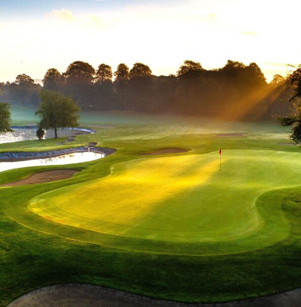 Morning sun over lush golf course, serene pond, and secluded green, ideal for a relaxing golfing getaway.