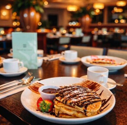 Sumptuous hotel breakfast with pancakes drizzled in chocolate, fresh strawberries, and steaming coffee in a cosy dining room.