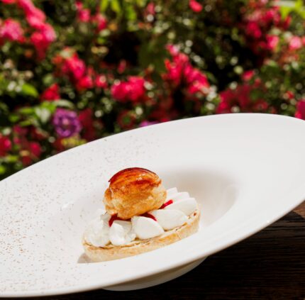 Delectable dessert on terrace with vibrant garden backdrop at luxury hotel.