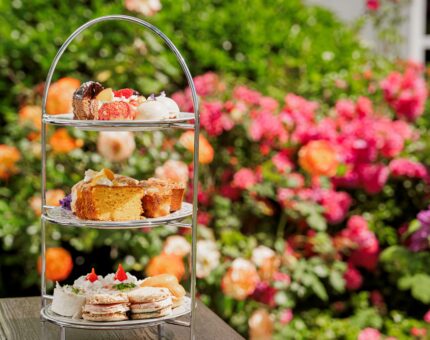 Afternoon tea stand with cakes and sandwiches on a garden table, vibrant flowers in the background.