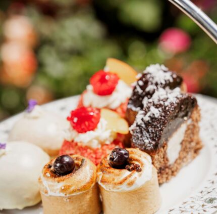Elegant afternoon tea with assorted pastries and cakes in a lush garden setting at luxury hotel.