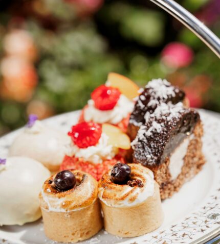 Elegant afternoon tea with assorted pastries and cakes in a lush garden setting at luxury hotel.