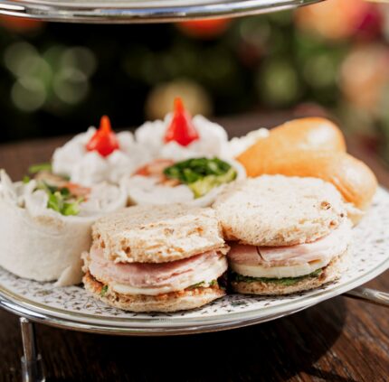 Elegant afternoon tea with assorted sandwiches and desserts at a luxury hotel, set on a wooden table.