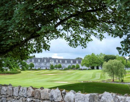 Luxury hotel with lush golf course views, framed by trees and serene landscape, perfect for relaxing retreats.
