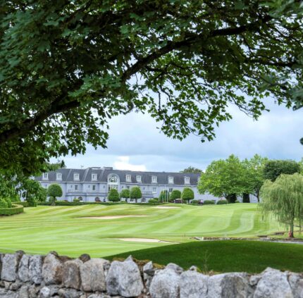 Luxury hotel with lush golf course views, framed by trees and serene landscape, perfect for relaxing retreats.