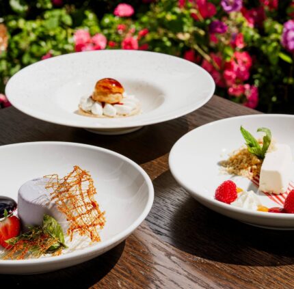 Elegant desserts on a wooden table against vibrant garden blooms at a luxury hotel, offering a delightful culinary experience.