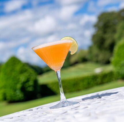 Vibrant cocktail with lime on sunny garden terrace at luxury hotel.