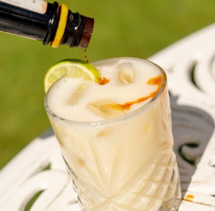 Refreshing cocktail with lime garnish on elegant white table in sunny hotel garden. Perfect for relaxation and leisure.