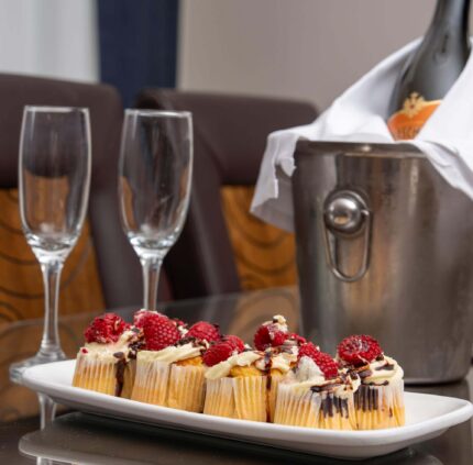 Luxurious hotel suite with champagne, glasses, and a plate of gourmet cupcakes on a polished table.