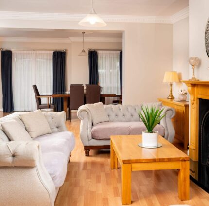 Spacious hotel suite with cosy sofas, elegant fireplace, and chic dining area, ideal for relaxing getaways.