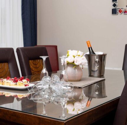 Elegant hotel dining area with a glass table set for wine and dessert, adorned with flowers, offering a luxurious stay.