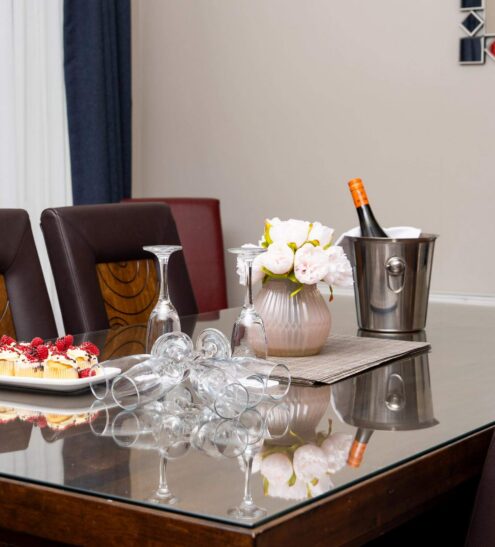 Elegant hotel dining area with a glass table set for wine and dessert, adorned with flowers, offering a luxurious stay.