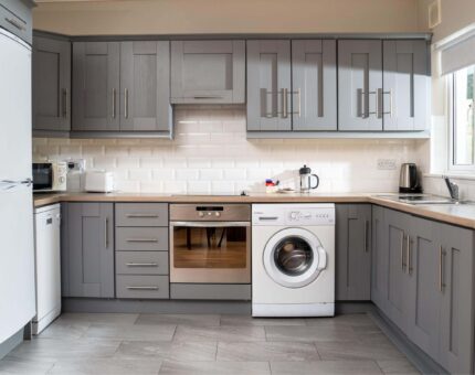 Modern hotel kitchen with grey cabinetry, fridge, oven, washing machine, and ample counter space for a comfortable stay.