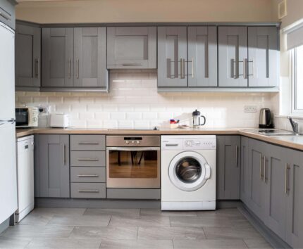 Modern hotel kitchen with grey cabinetry, fridge, oven, washing machine, and ample counter space for a comfortable stay.