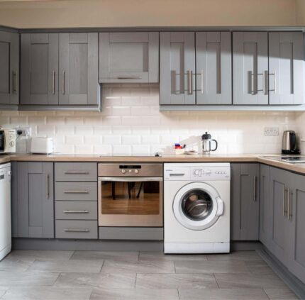 Modern hotel kitchen with grey cabinetry, fridge, oven, washing machine, and ample counter space for a comfortable stay.