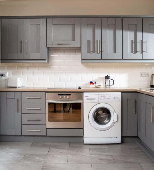 Modern hotel kitchen with grey cabinetry, fridge, oven, washing machine, and ample counter space for a comfortable stay.
