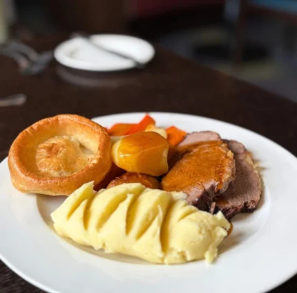 Savour a traditional British roast with tender beef, Yorkshire pudding, roast potatoes, and carrots in a cosy dining setting.